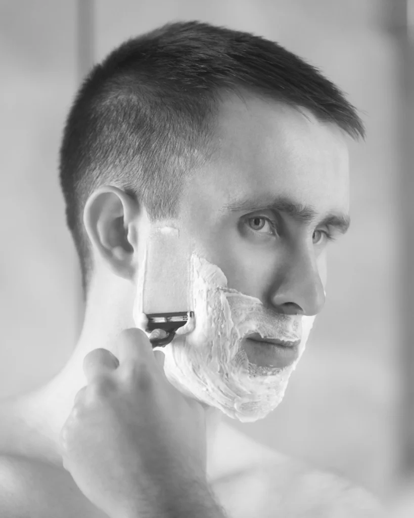 Man shaving his face in the mirror, showing the daily skin irritation many men try to avoid by growing a beard