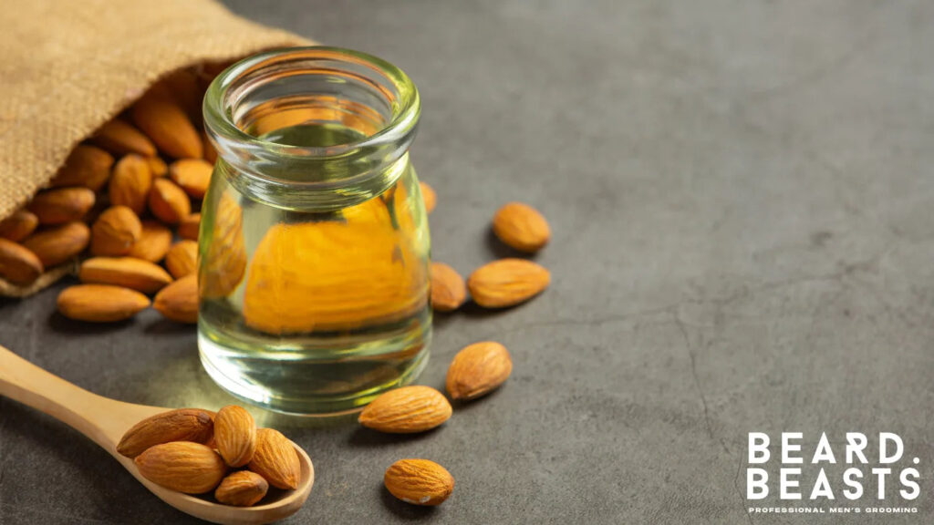 Glass jar of sweet almond oil with raw almonds on a dark surface, a lightweight carrier oil for beard care and sensitive skin.