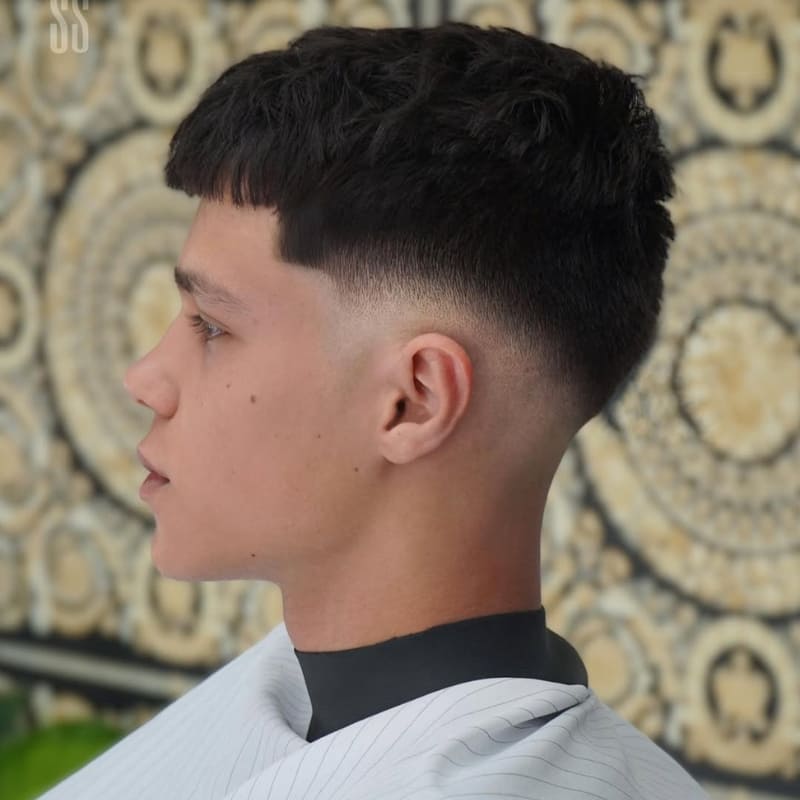 Blunt fringe French crop with mid fade featuring a straight-cut fringe and tight skin fade—an edgy, low-maintenance men's haircut ideal for straight hair and defined facial features.