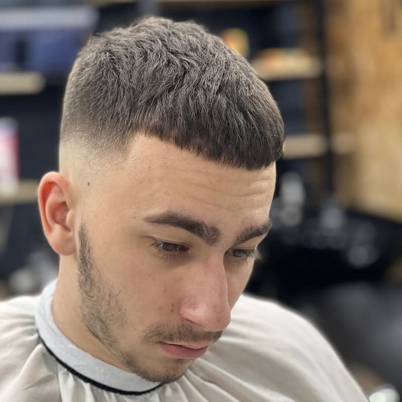 Man with a classic French crop mid fade haircut featuring a short textured top, blunt fringe, and clean mid fade on the sides — a popular low-maintenance men’s hairstyle