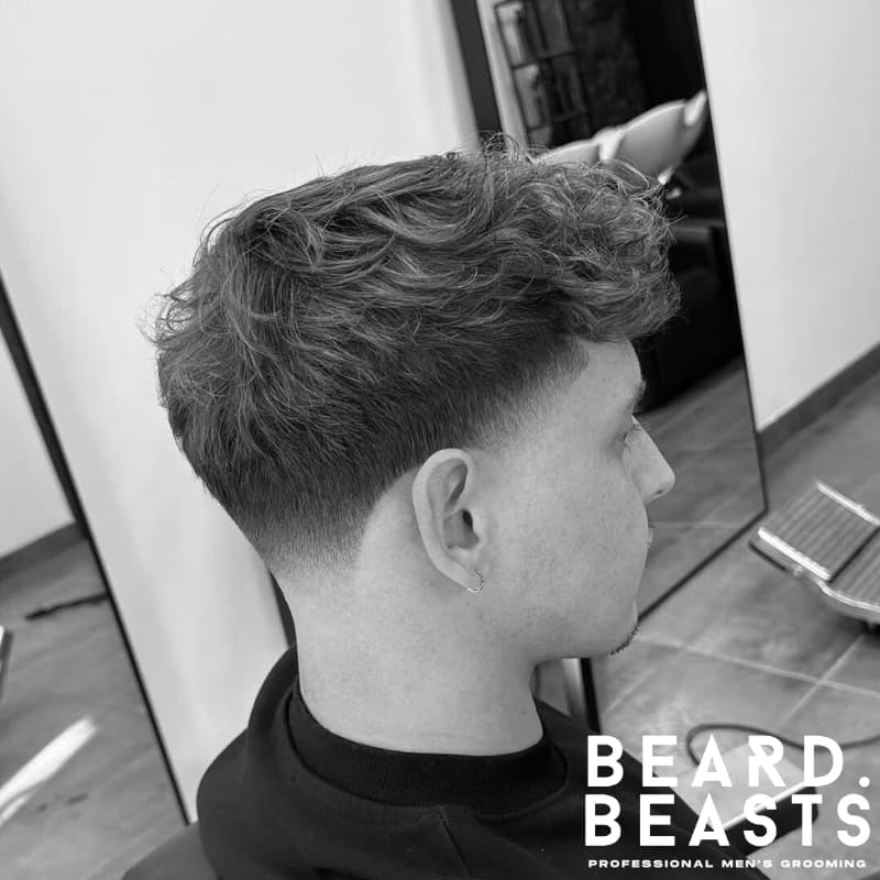 Side view of a man with a wavy fringe and clean taper fade, highlighting one of the most stylish fringe haircuts for men with natural volume