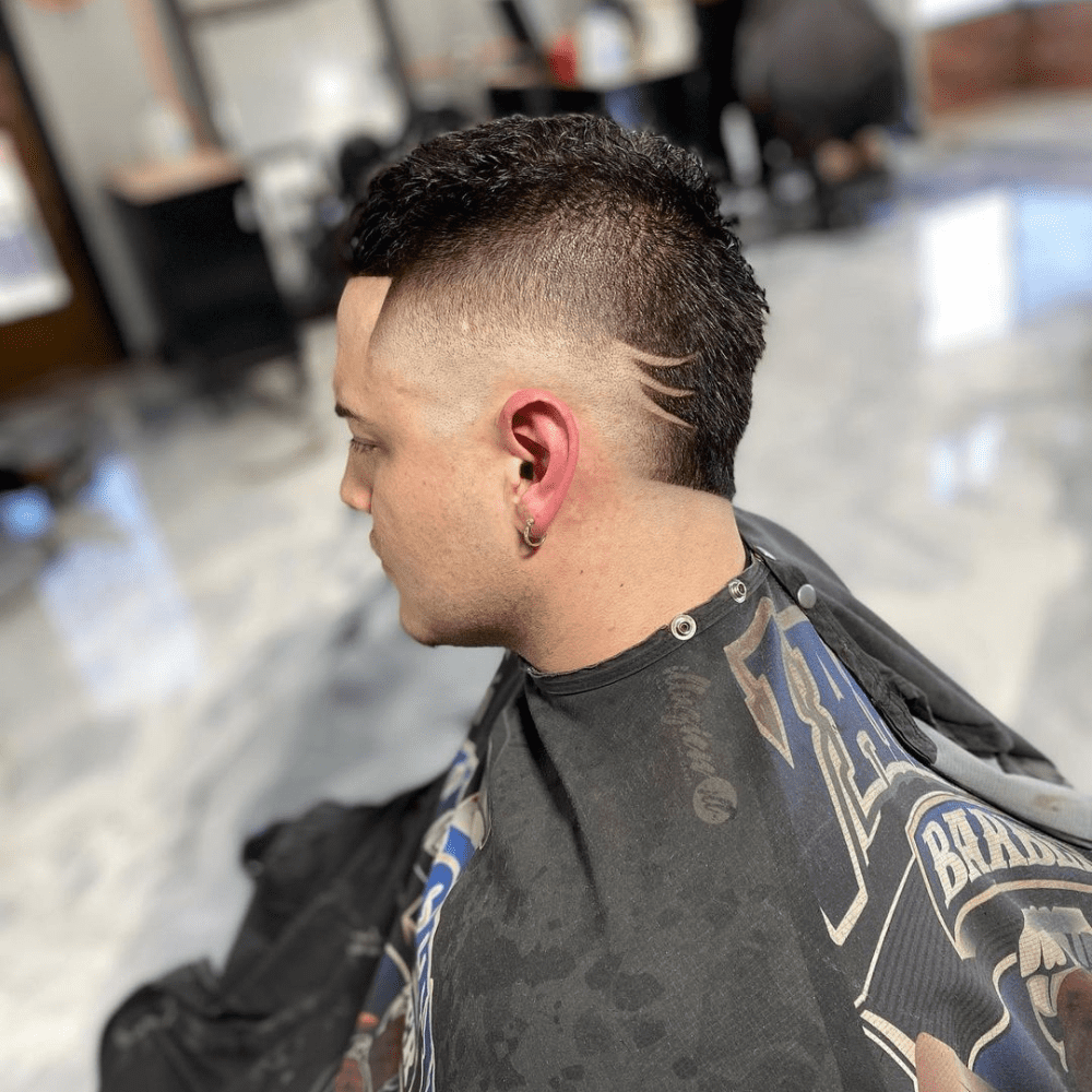 Mohawk Fade featuring a textured top, a sharp high fade, and three curved lines shaved into the side design.