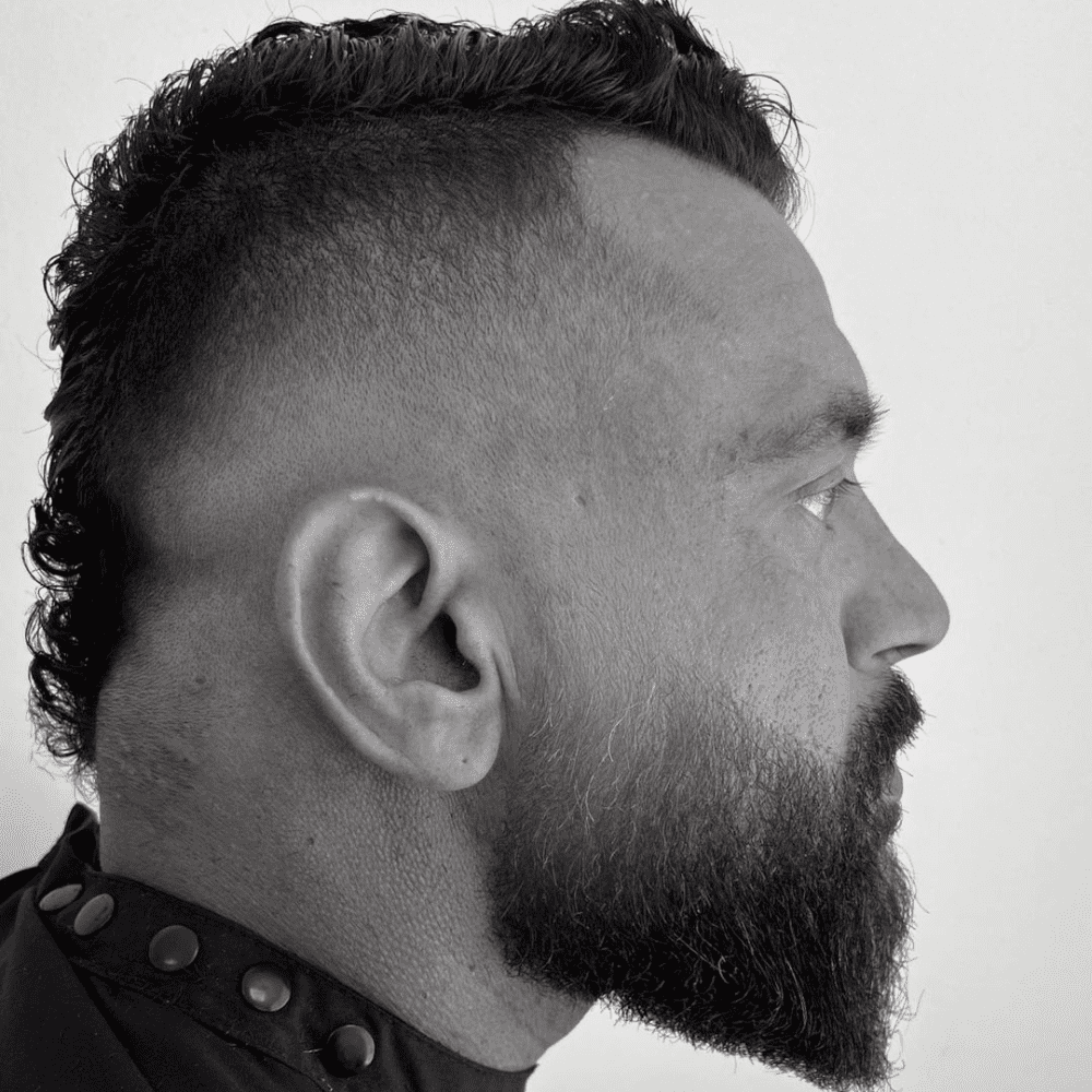 Mohawk Fade featuring a sharp, high fade on the sides, a textured top, and a full, well-groomed beard.