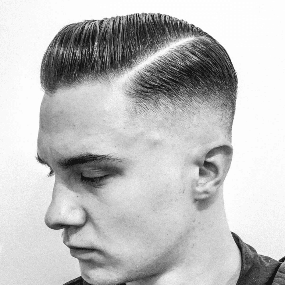 A close-up profile shot of a young man with a classic haircut. The style features a high skin fade on the sides, a sharp razor side part, and the longer hair on top combed over neatly.