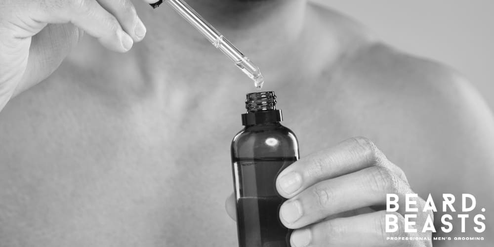 Man using a dropper to apply beard oil from a dark glass bottle, featuring the Beard Beasts logo in the corner. Professional men's grooming product.