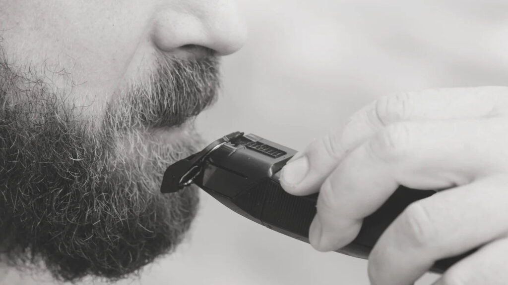 Close-up of man trimming beard with electric clipper to avoid common beard trimming mistakes