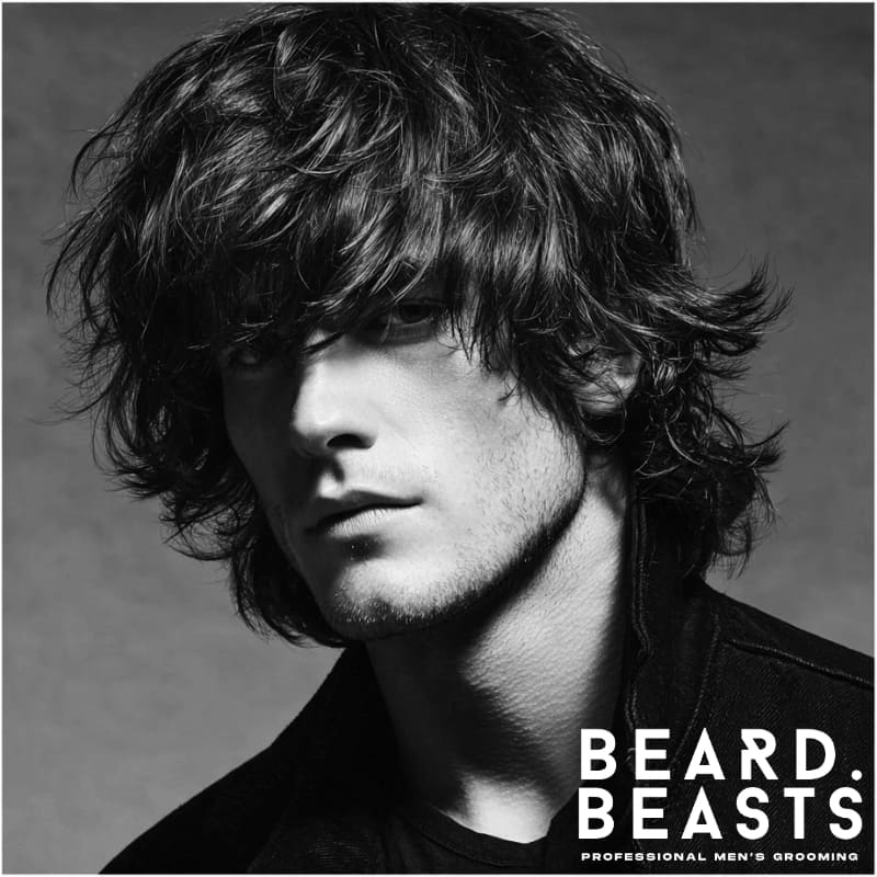 Men's shaggy hairstyle featuring textured, layered hair with a voluminous, messy look. The hair is styled with uneven layers and choppy ends, creating a carefree, tousled appearance.