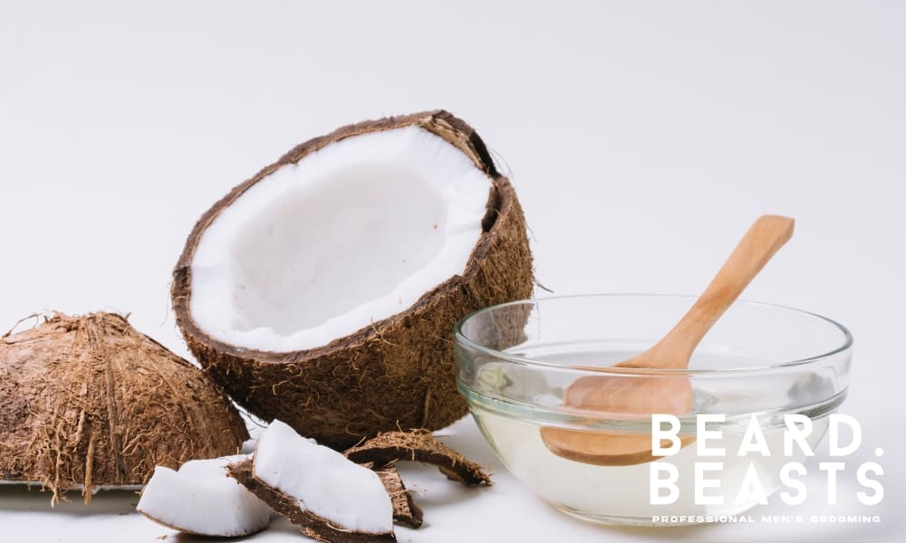 Close-up of coconut oil in a glass bowl with a wooden spoon, next to fresh coconut halves and slices—an effective natural hair clipper oil alternative