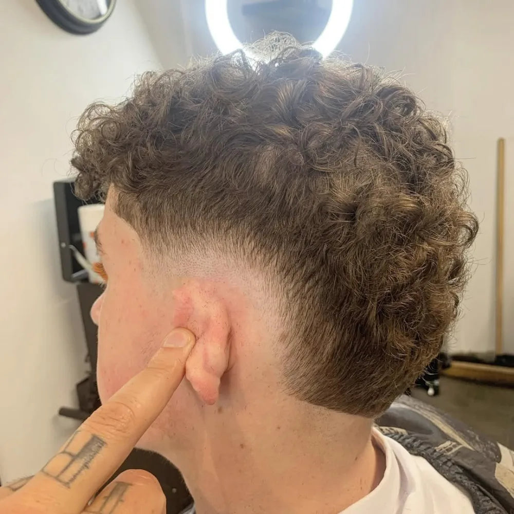 Man with a curly burst fade haircut, featuring tightly faded sides that curve around the ear and textured curls left longer on top.