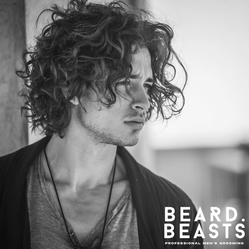 Male model with a curly men's flow haircut, featuring natural curls and volume for a stylish, effortless look.