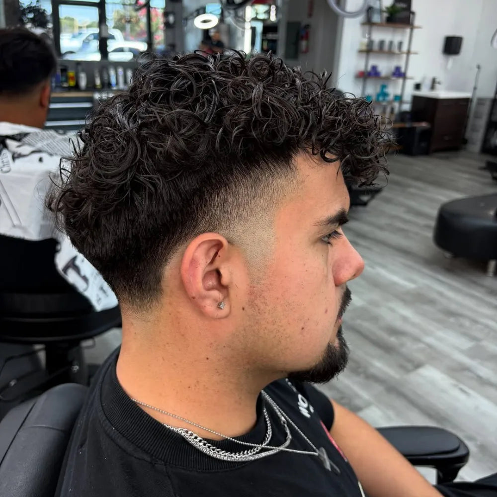 Man with a curly high taper fade haircut, featuring gradually shortened sides around the temples and neckline with defined curls on top.