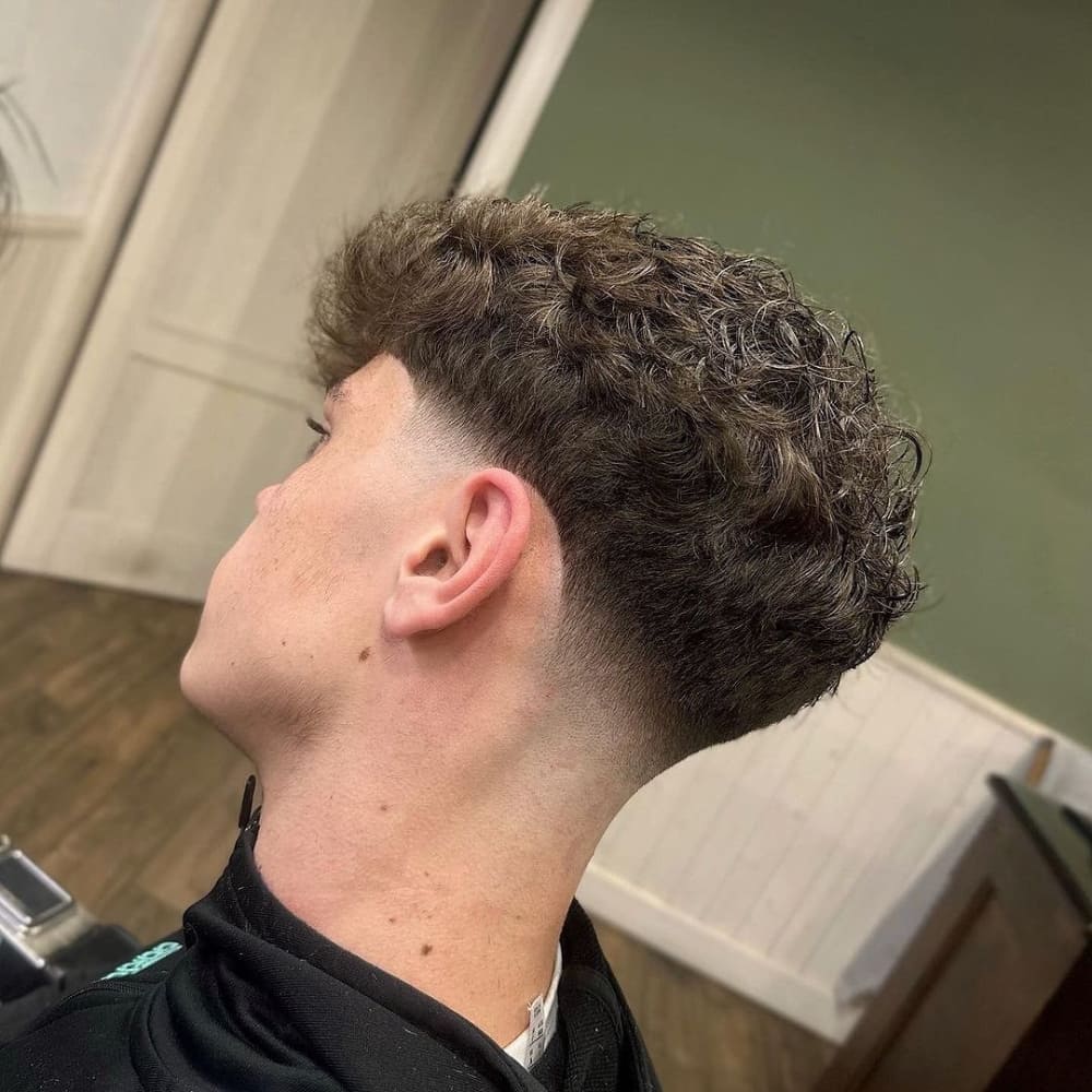 Man with a curly top low fade haircut, featuring naturally curly hair on top and a clean fade on the sides and back, presenting a stylish and modern look.