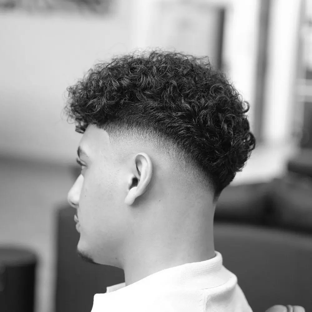 Man with natural curly hair and a mid drop fade, featuring a sharp fade that curves behind the ears and blends cleanly into the skin for a modern, defined look.