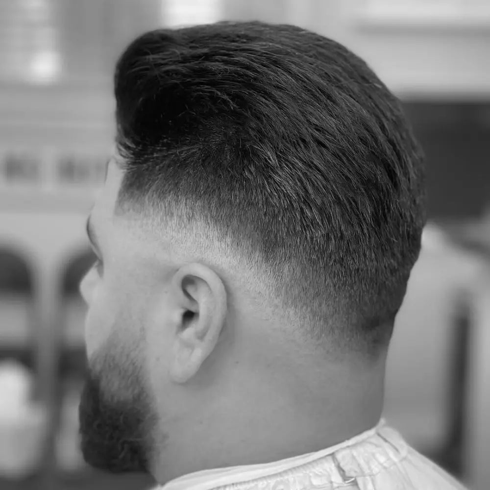 Man with a drop fade and pompadour hairstyle, featuring a defined fade that curves behind the ear and blends smoothly into voluminous, styled hair on top.