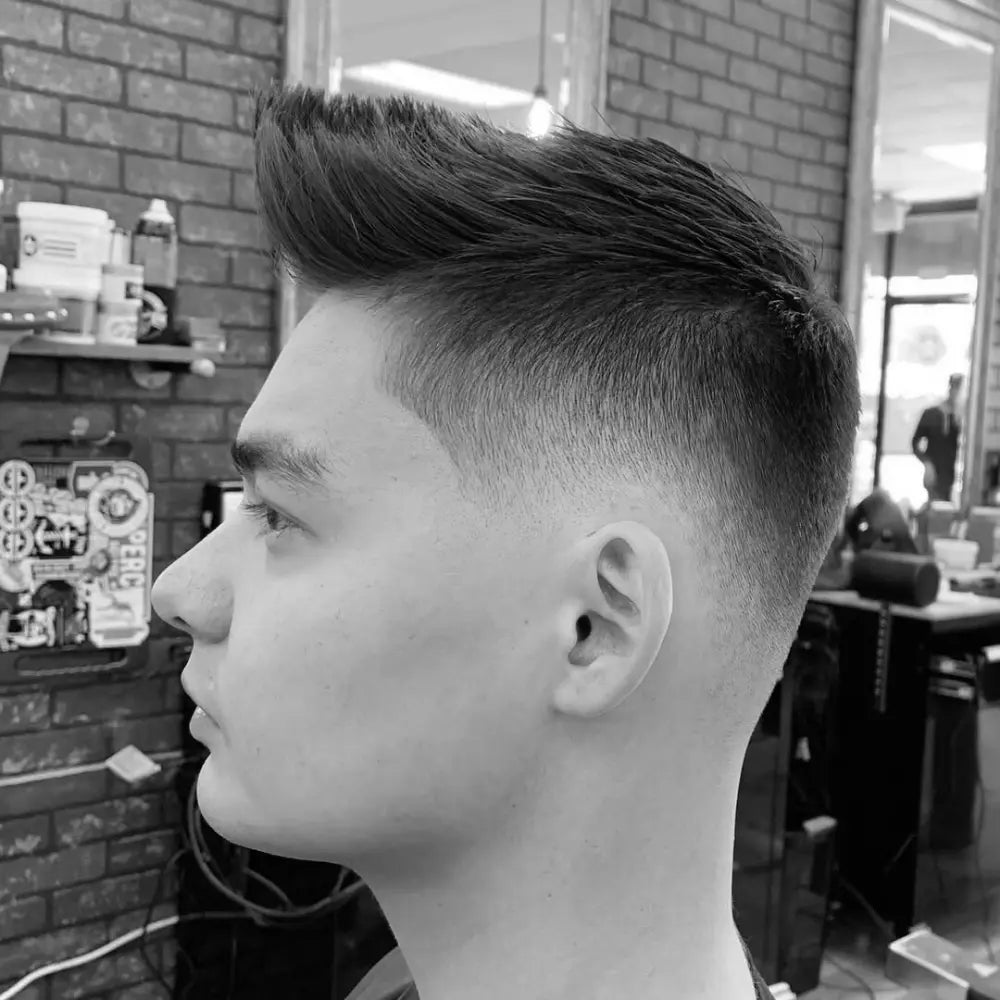 Man with a textured faux hawk and drop fade, featuring a sharp fade that curves behind the ears and blends seamlessly into the skin for a bold, modern haircut.