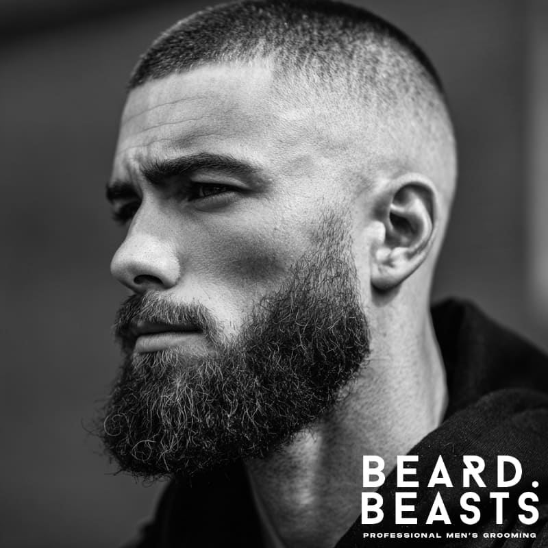 A clean faded buzz cut paired with a full, well-groomed beard, creating a sharp and defined look. The contrast between the short, neatly faded hair and the fuller beard adds depth, offering a bold, masculine style with a strong, structured appearance.