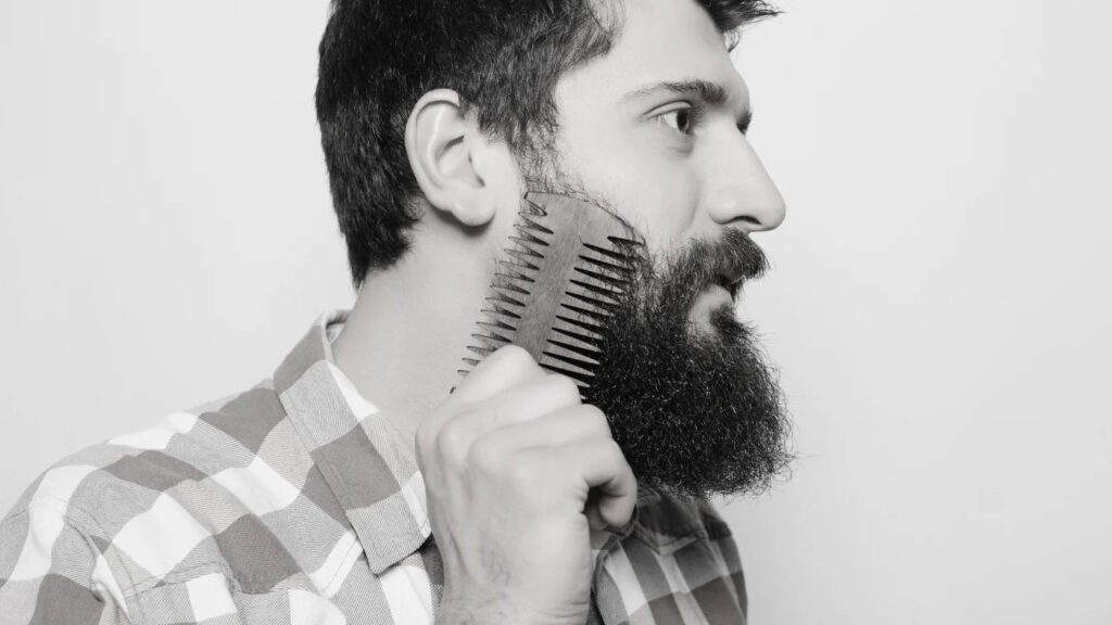 Man combing his thick beard with a wooden comb to prevent uneven cuts and avoid beard trimming mistakes