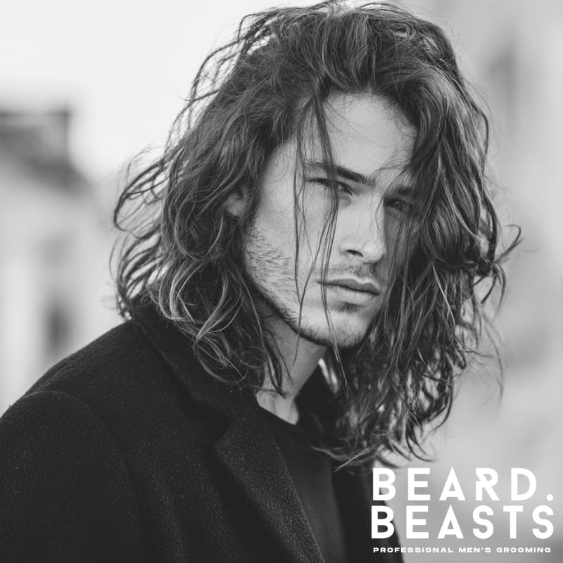 Handsome male model with a long men's flow haircut, featuring loose, natural waves and effortless volume.