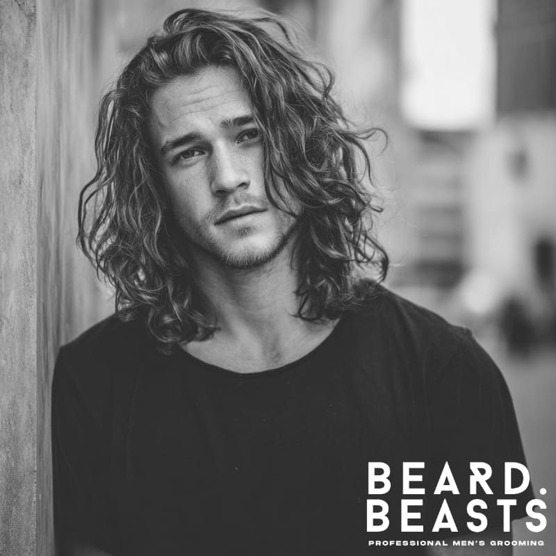 A man with long, naturally wavy hair styled in loose waves, offering a relaxed and textured look. Ideal for those looking for effortless, modern hairstyles for men with long hair that highlight natural volume and movement.