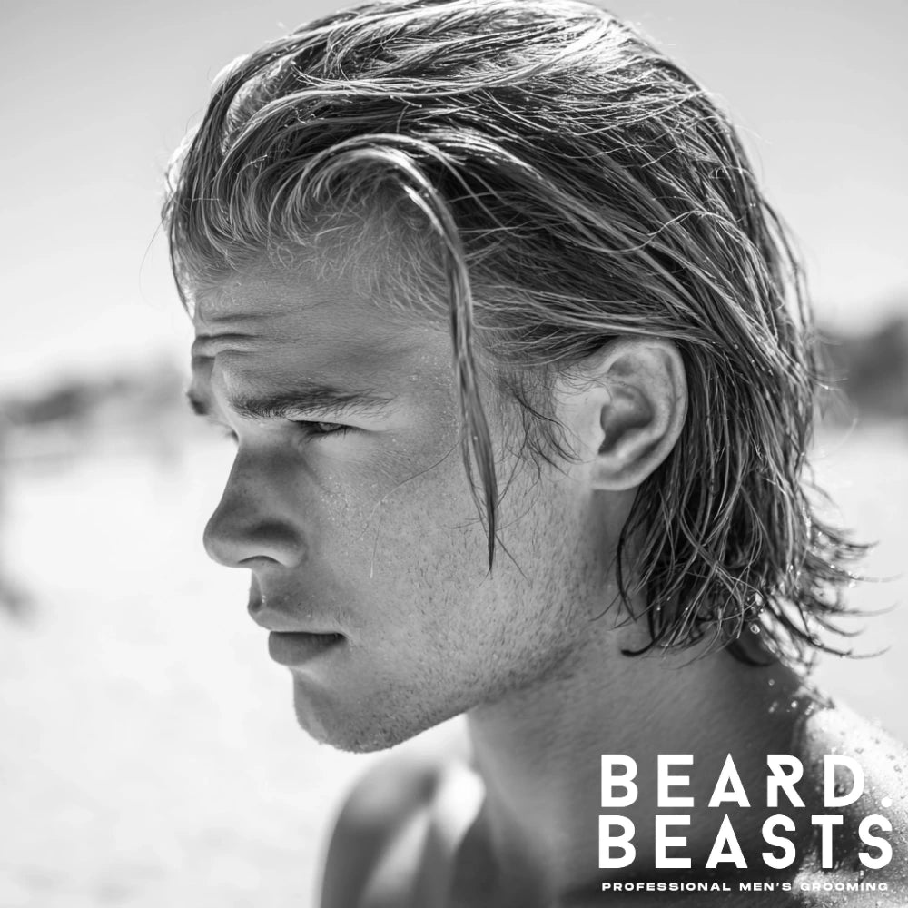 Man with long slicked back surfer hairstyle, wet hair glistening under the sun on the beach