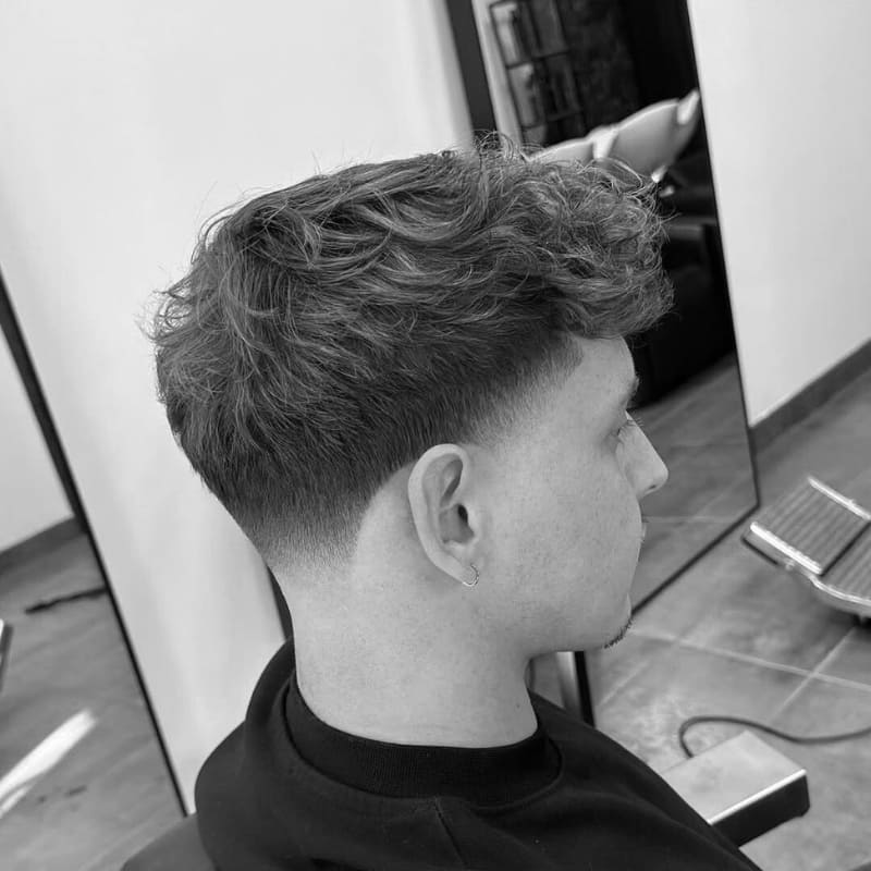 Young man with soft layers on top and a low fade on the sides, creating a clean, polished look with a subtle contrast.