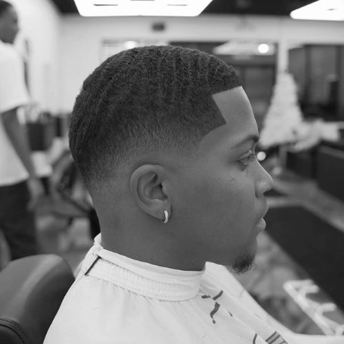 A black and white image of a black man's fresh low fade haircut with defined waves.