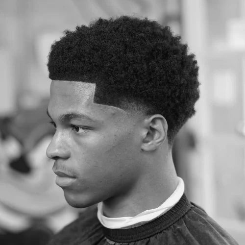 A stylish low taper fade haircut for Black men, featuring a clean, gradual fade that blends seamlessly into the textured afro top. The crisp lineup enhances the sharp and polished look, making this fade haircut a perfect choice for those who want a modern yet natural style.