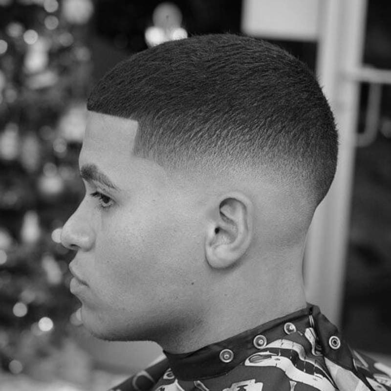 Side profile of a man with a low fade buzz cut, featuring a clean skin fade that starts just above the ears and blends seamlessly into short, even hair on top. A sharp, low-maintenance low fade haircut for men with straight hair.