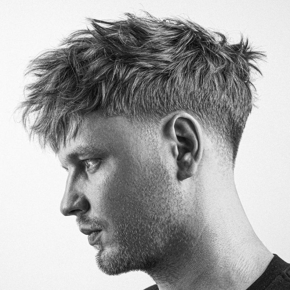Man with a low fade messy top haircut, featuring textured, tousled hair on top and a clean fade on the sides and back, showcasing a modern, trendy appearance.