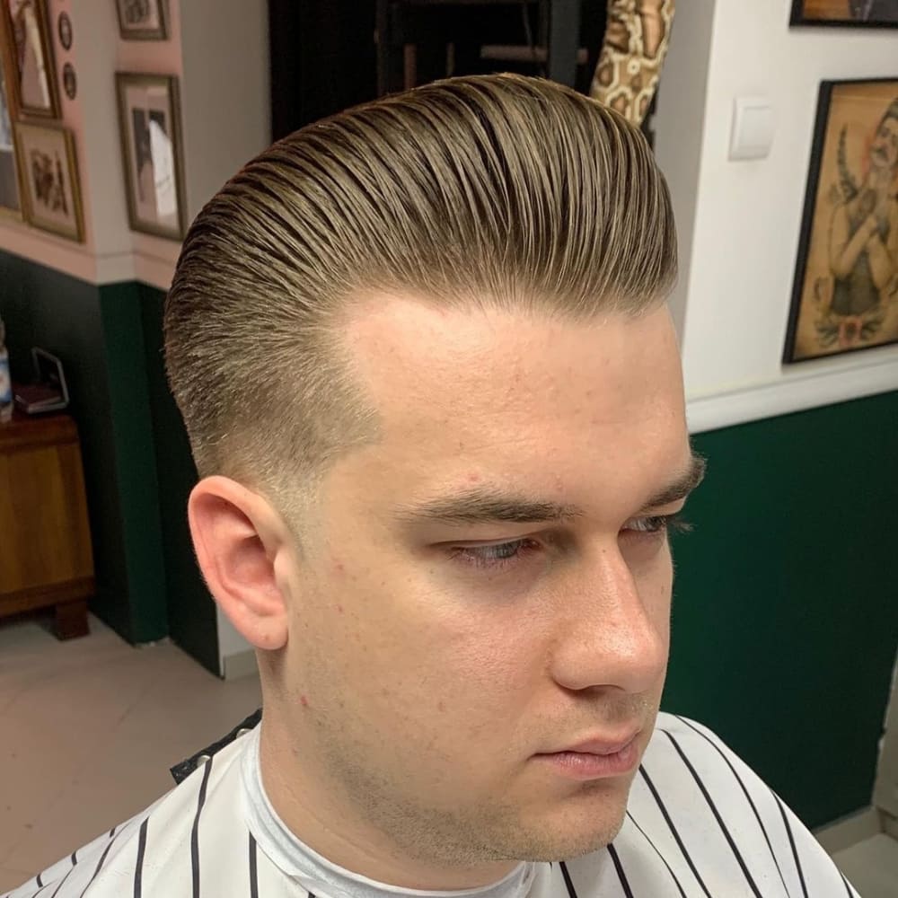 Man with a low fade pompadour haircut, featuring a sleek, voluminous top and cleanly tapered sides, presenting a bold yet refined style.