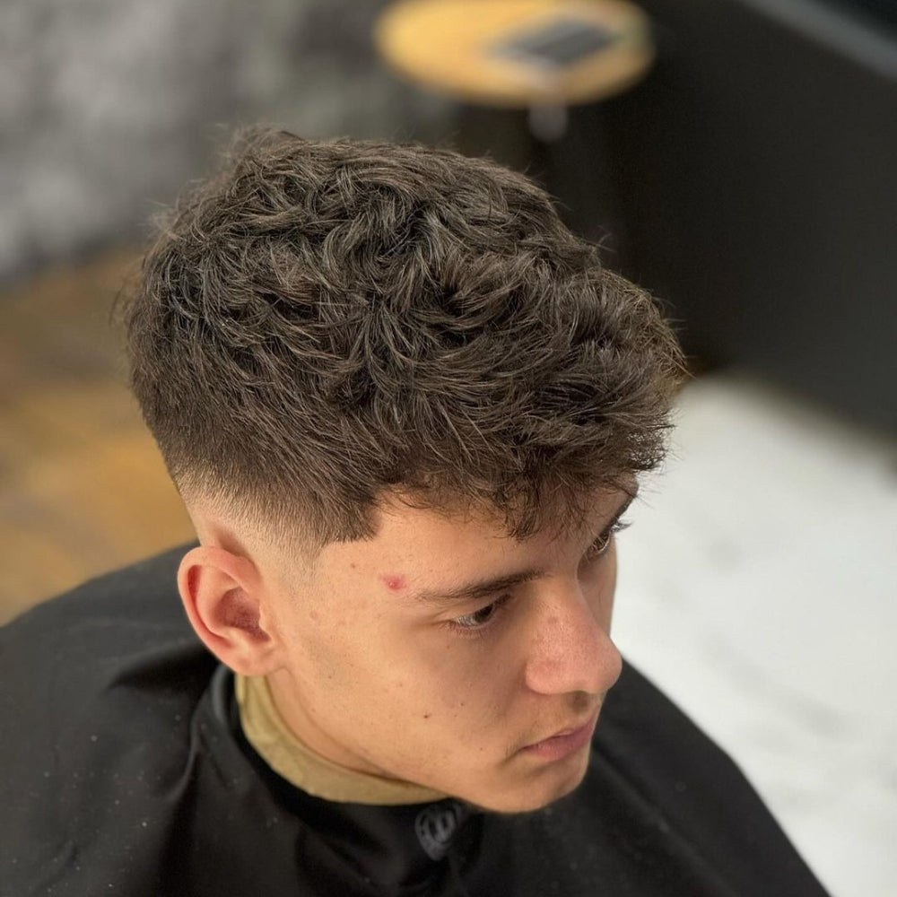 Man with a low fade haircut and textured top, featuring short, cleanly faded sides and back with a voluminous, textured hairstyle on top, delivering a trendy and modern look.