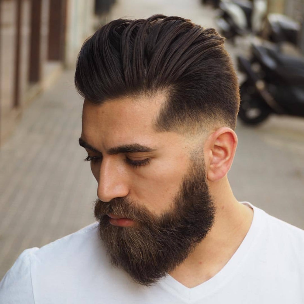 Man with a low fade haircut and full beard, featuring a sleek, voluminous top paired with a sharp fade and a thick, well-groomed beard, showcasing a stylish and masculine look.