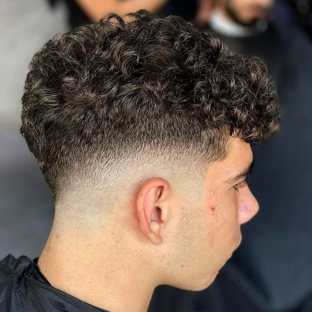 Young man with a low fade haircut featuring naturally curly hair, delivering a clean and stylish look suitable for various hair types and face shapes.