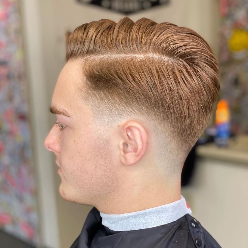 Man with a low skin fade combover haircut, featuring neatly combed-over hair on top with a clean fade down to the skin on the sides and back, showcasing a stylish and professional look.