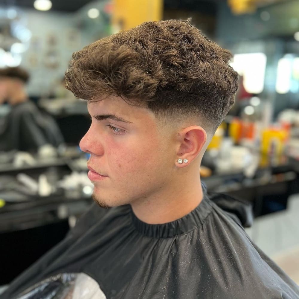 Man with a low fade haircut for thick hair, featuring voluminous, naturally curly hair on top and a clean, gradual fade on the sides, showcasing a stylish and contemporary look.