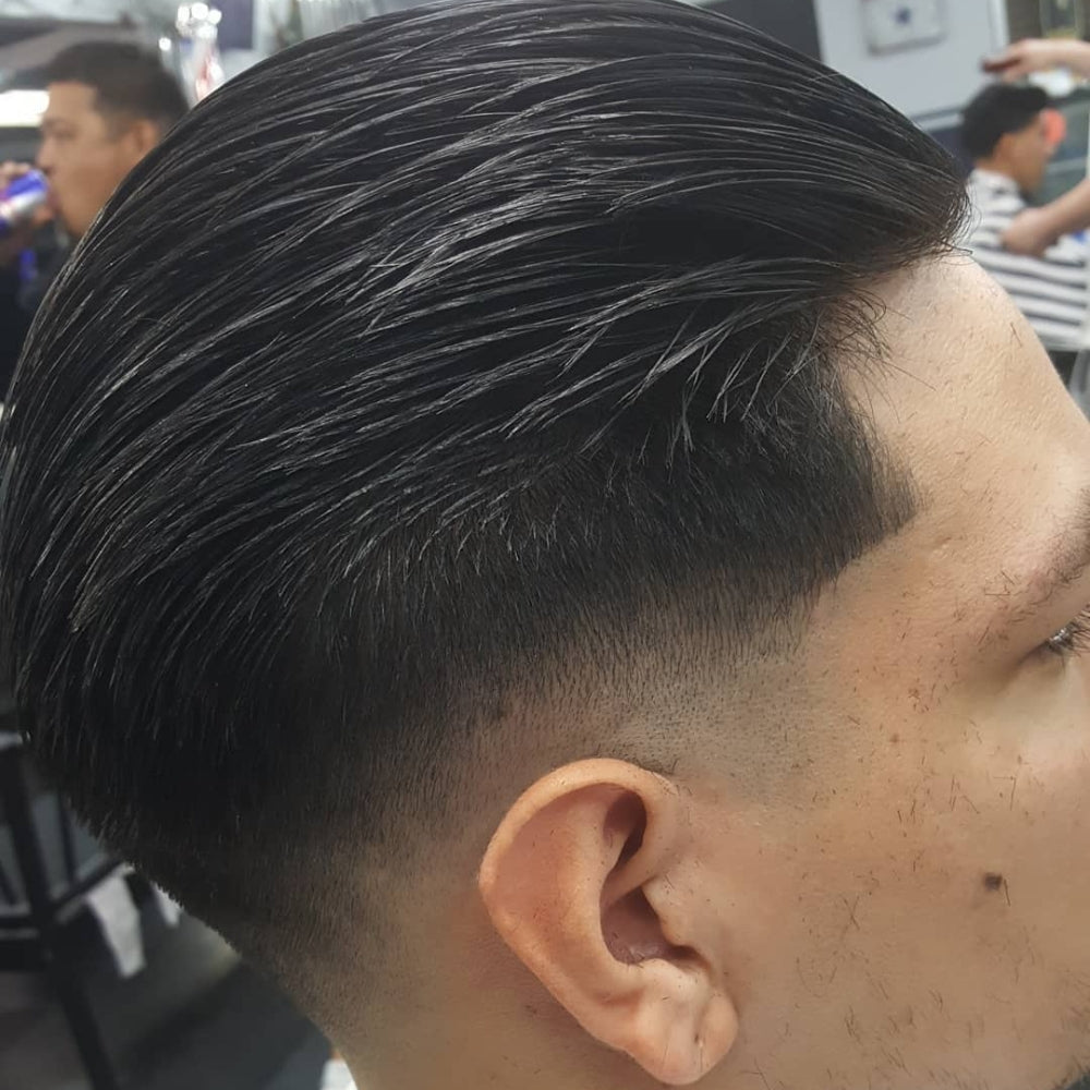Man with a low skin fade slick back haircut, featuring sleek, combed-back hair on top and a clean, sharp fade on the sides, delivering a polished and contemporary style.