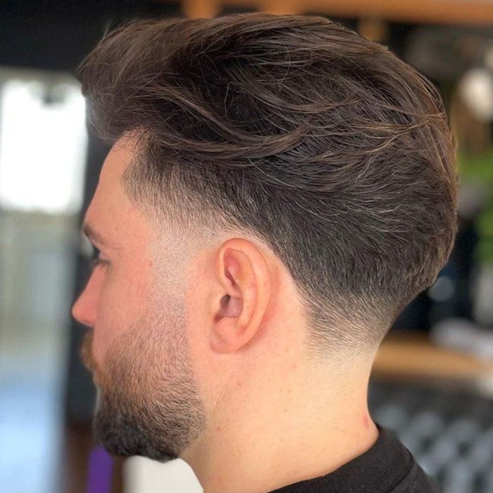 Man with a low fade taper haircut, featuring a smooth, gradual fade on the sides and back with longer, textured hair on top, delivering a sophisticated and versatile style.