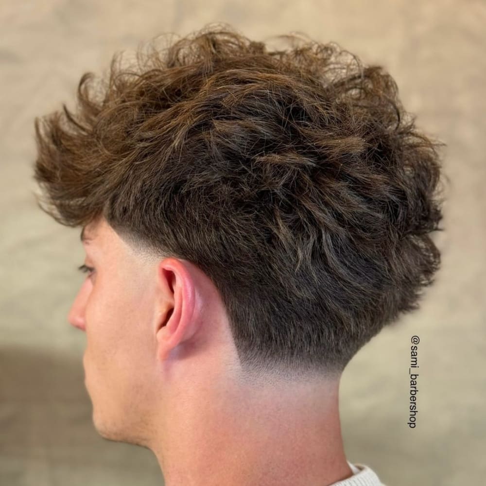 Man with a low taper fade and long top haircut, featuring voluminous, textured hair on top and a clean, gradual fade on the sides, creating a stylish and contemporary appearance.