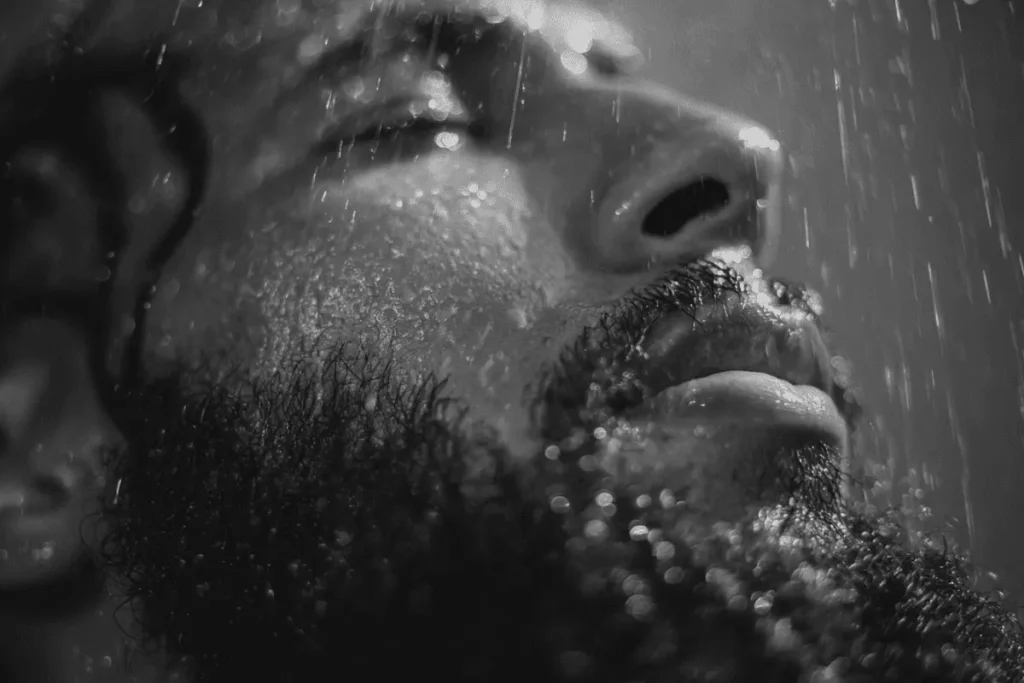 Close-up of a man rinsing a wiry beard under warm water
