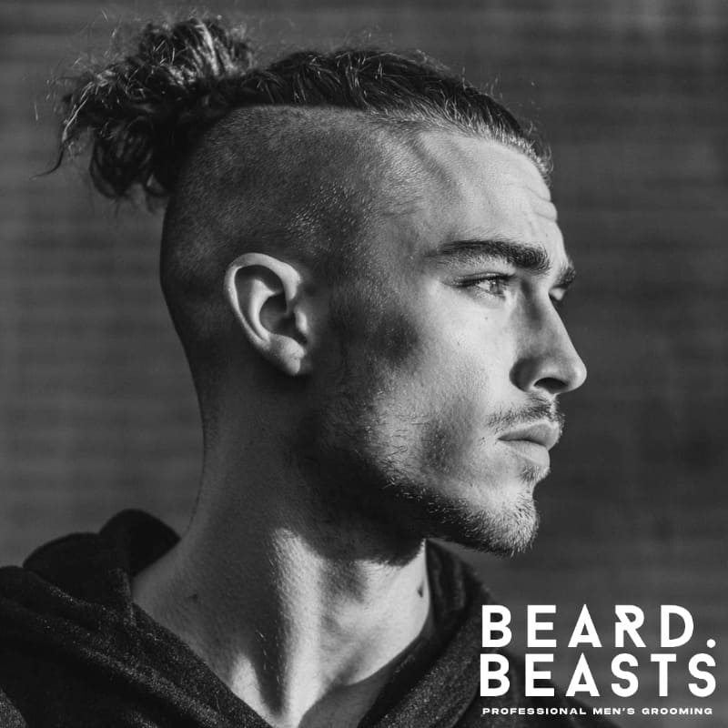 A man with naturally curly hair styled in a top knot, paired with a clean fade on the sides. This bold, modern look is perfect for those seeking inspiration for men’s hairstyles with long hair and sharp fades.