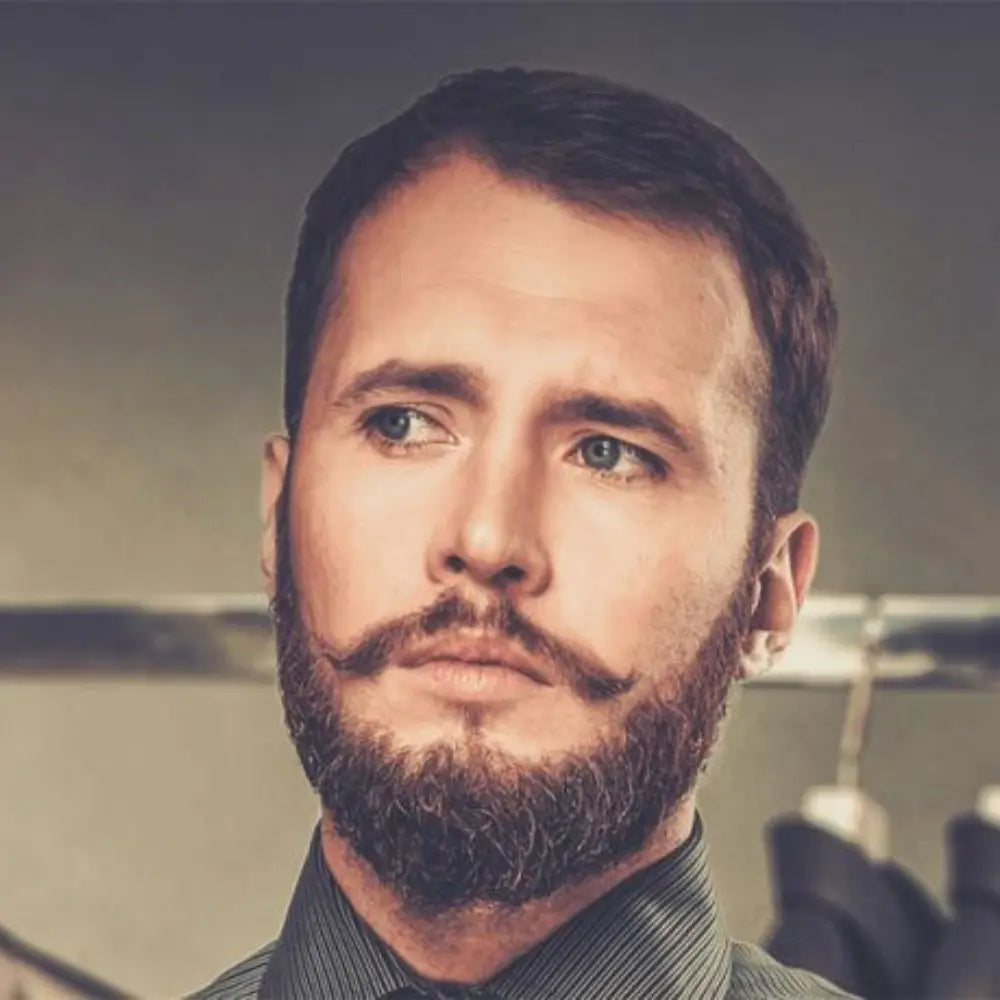 Man with a Verdi beard style featuring a curled mustache and medium-length beard, dressed in a formal shirt.