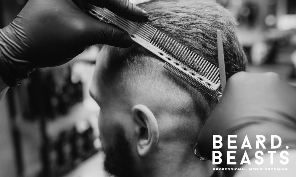 A close-up shot of a man receiving a haircut from a barber. The barber, wearing black gloves, is using a comb to carefully trim the hair on the sides of the man's head. The image highlights the precision and attention to detail in the hair grooming process.