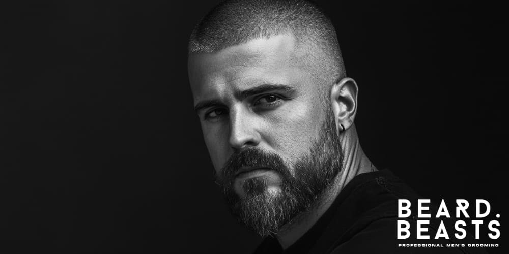 A striking black-and-white image of a bearded man with a number 4 buzz cut, showcasing a clean and bold look. The man's intense gaze and well-groomed beard complement the sharp lines of his hairstyle.