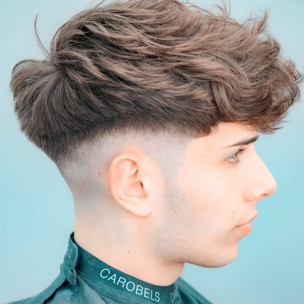 A young man with a textured French crop mid fade haircut, featuring a voluminous top and sharp fade for a stylish and modern look.