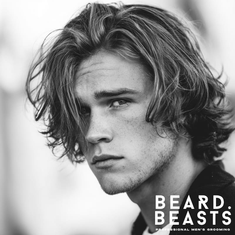 Handsome male model with a medium-length men's flow haircut, featuring natural waves and volume for a relaxed, tousled look.
