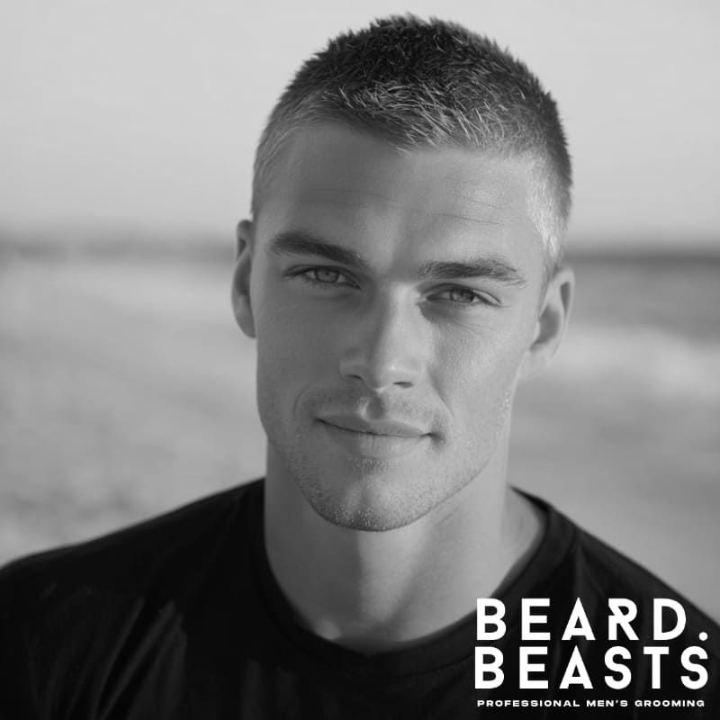 Portrait of a male model with a neat, short crew cut hairstyle, with a subtle golden hue from the sunset, on a beach background.