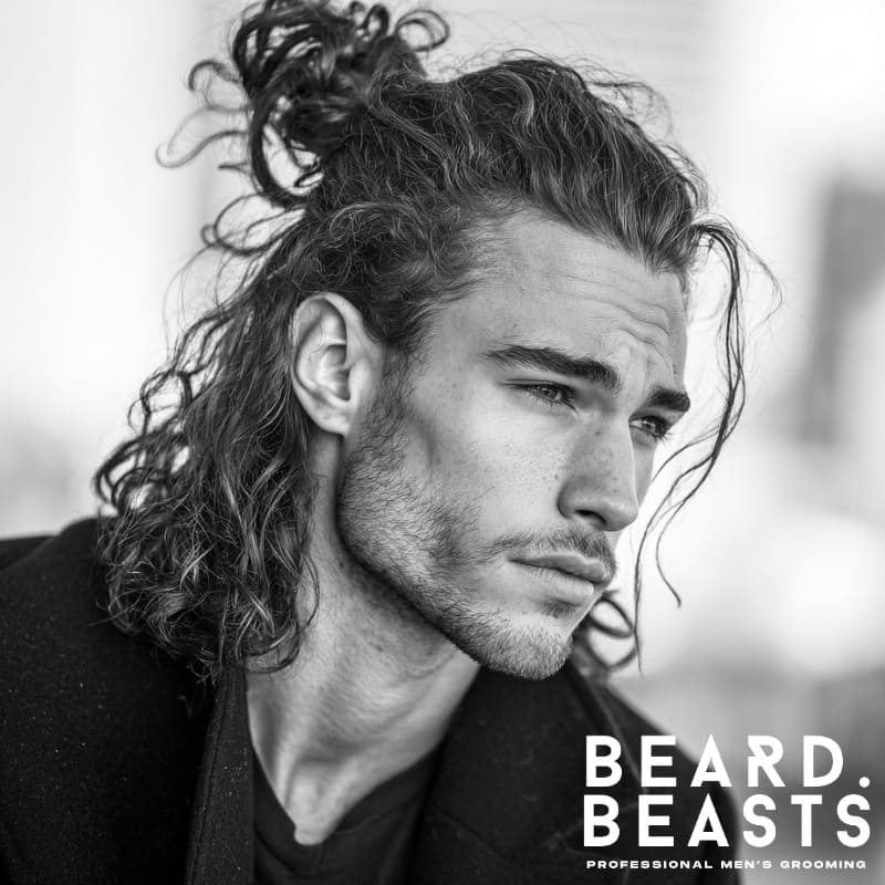 A man with naturally curly hair styled in a trendy half-up, half-down look. Perfect for those looking for a versatile and modern hairstyle that combines casual ease with a refined, structured appearance.