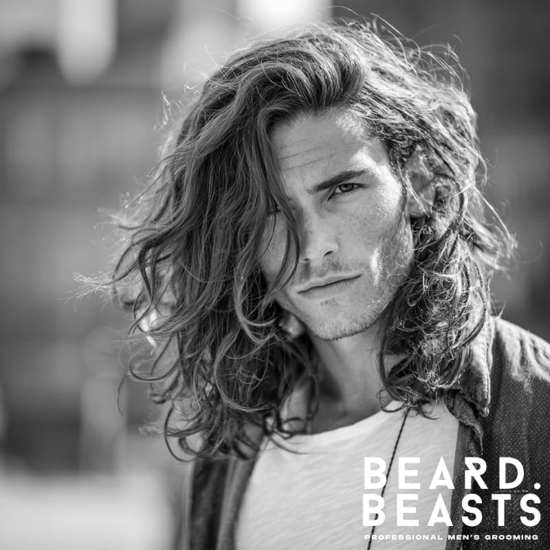 A stylish man with long, naturally textured hair, featuring soft layers that add volume and movement. Perfect for those seeking a versatile, modern men’s hairstyle with a relaxed yet polished look.