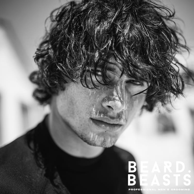 Close-up of a male model with a textured, messy fringe haircut, showcasing windswept hair falling over the forehead in a casual surfer style.