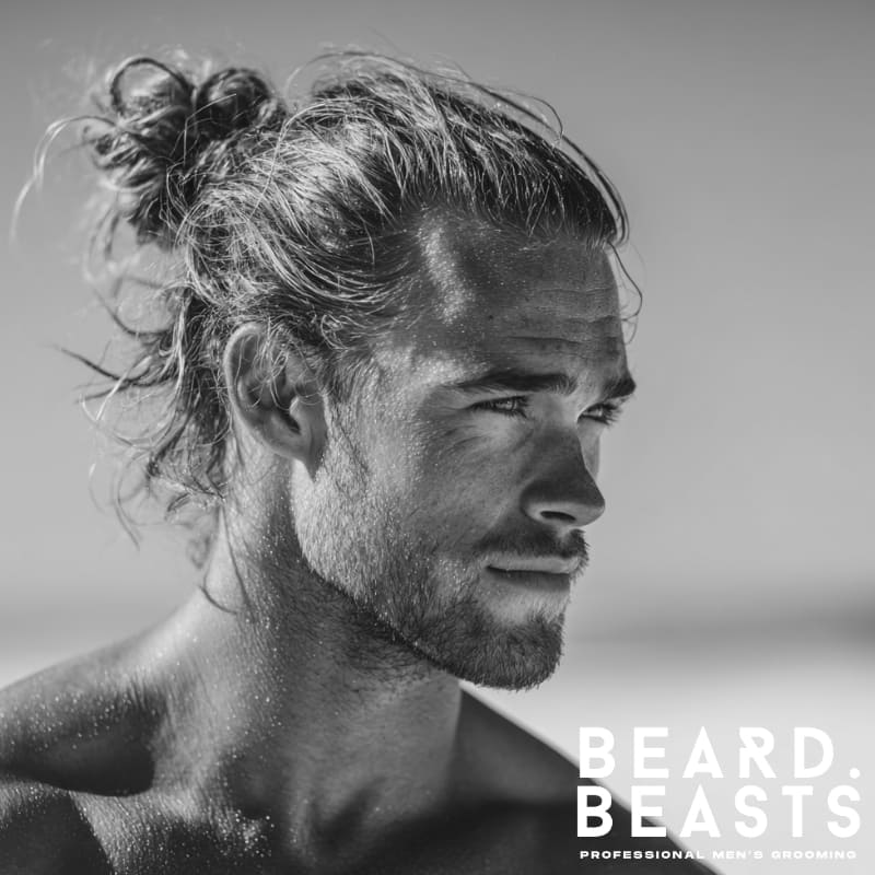 Handsome male model with a messy man bun, showcasing a relaxed and practical surfer hairstyle on the beach.